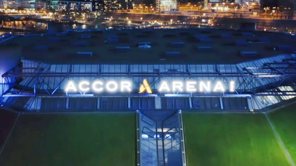 Vue aérienne nocturne de l’extérieur de l’Accor Arena, avec son enseigne illuminée et les lumières de la ville en arrière-plan.