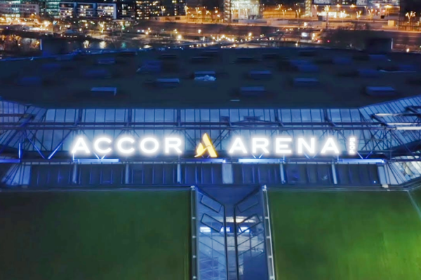 Vue aérienne nocturne de l’extérieur de l’Accor Arena, avec son enseigne illuminée et les lumières de la ville en arrière-plan.